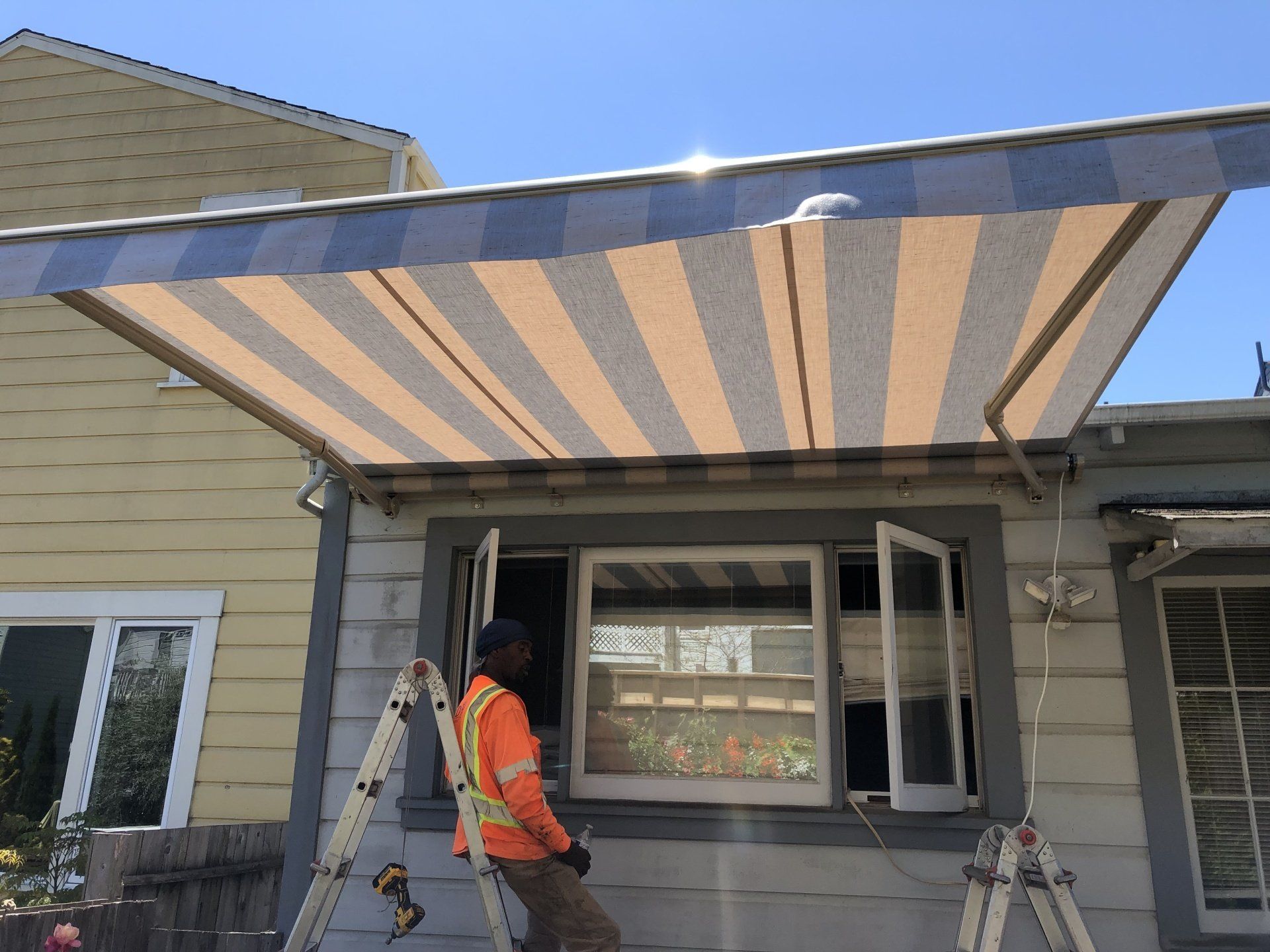 A man is standing on a ladder under an awning on the side of a house.