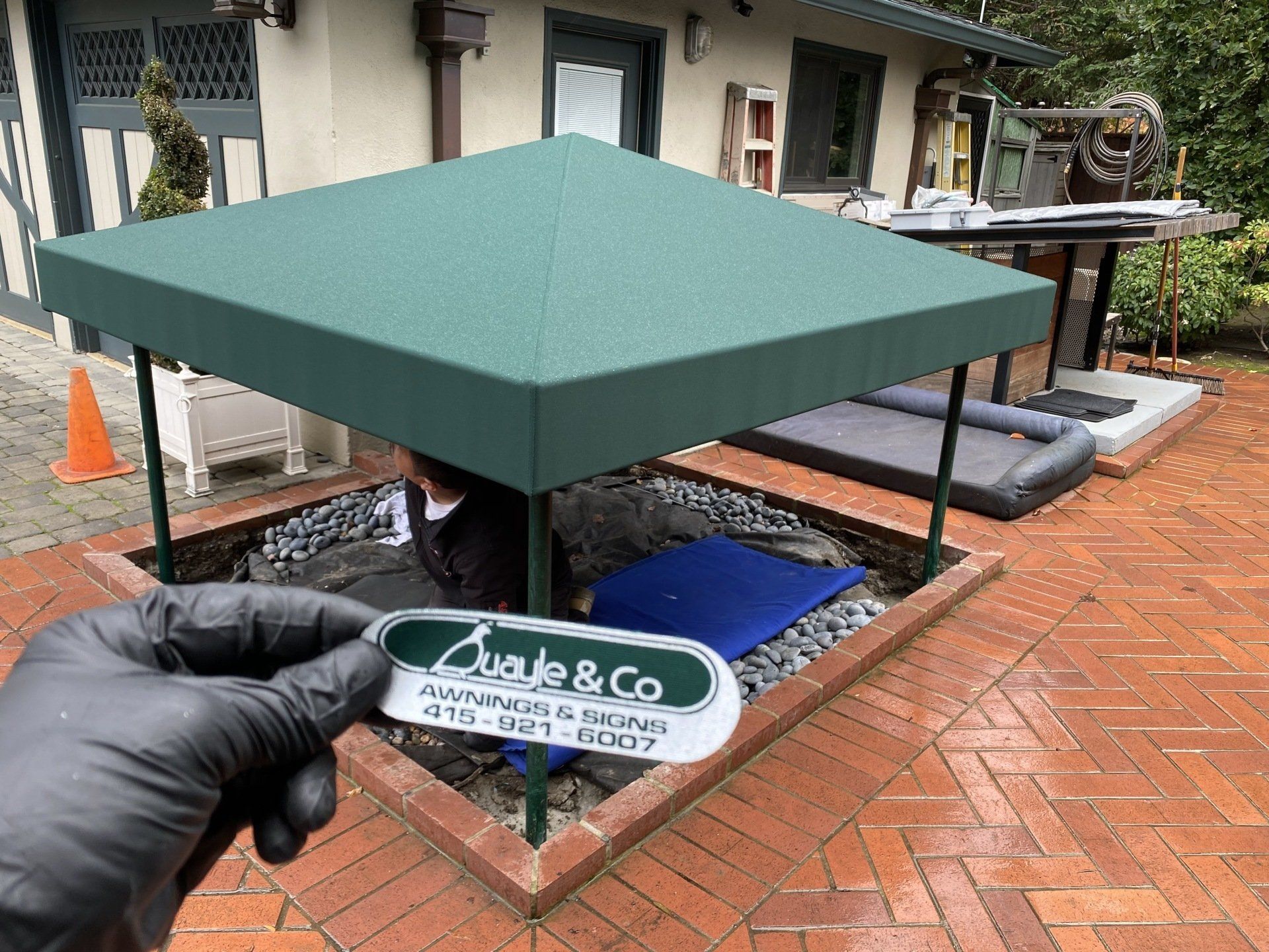 A person wearing black gloves is holding a business card in front of a green canopy.