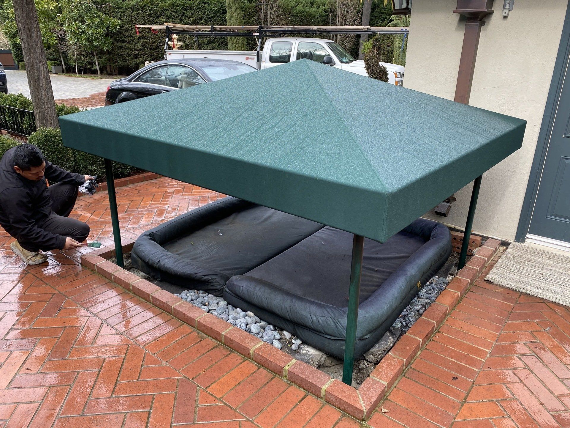 A man is kneeling under a green canopy over a dog bed.