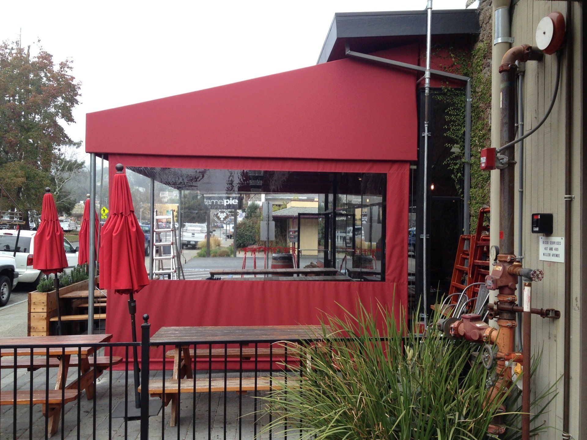 A red awning is covering a patio area with tables and umbrellas