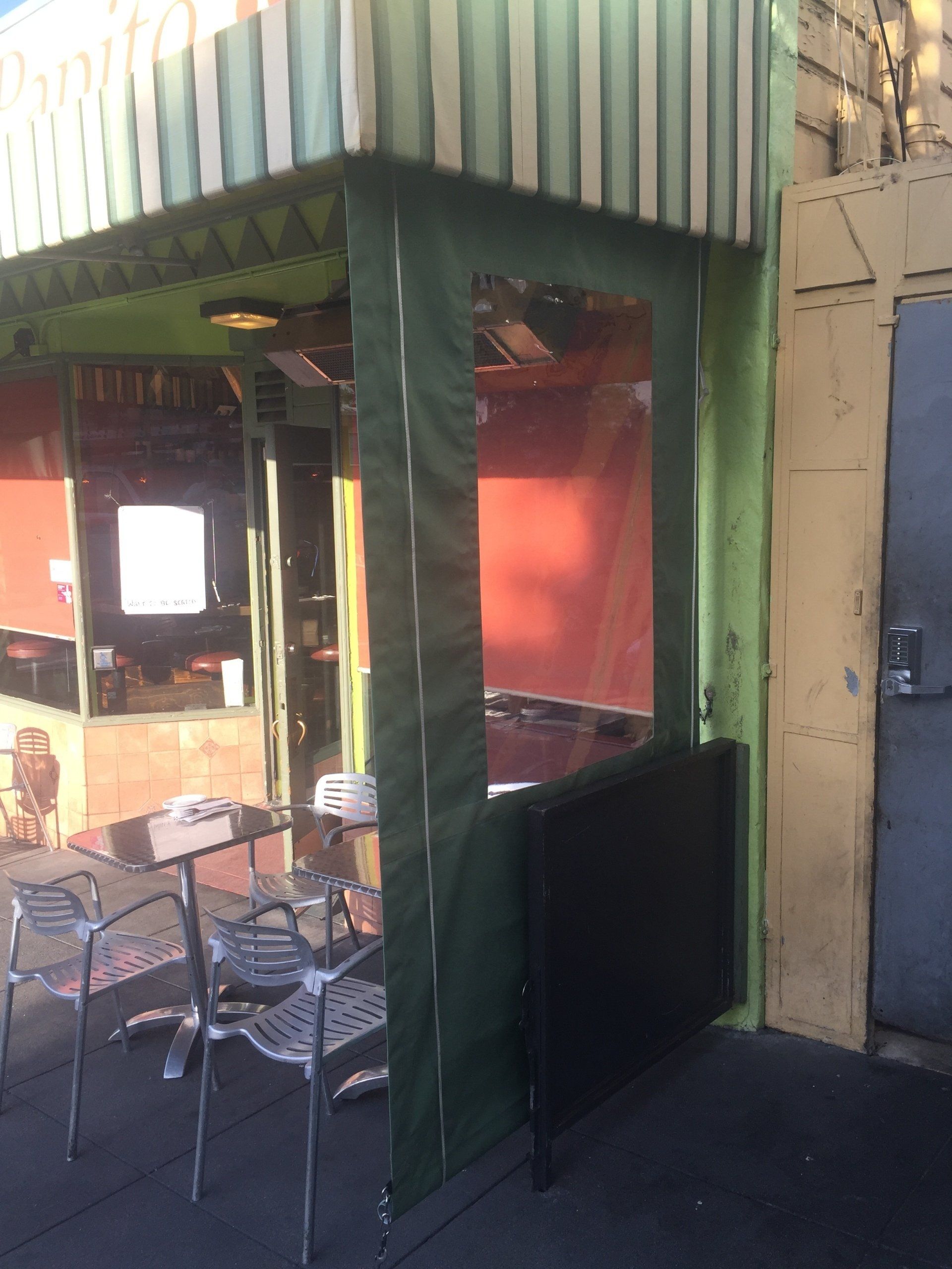 A restaurant with tables and chairs under a green awning