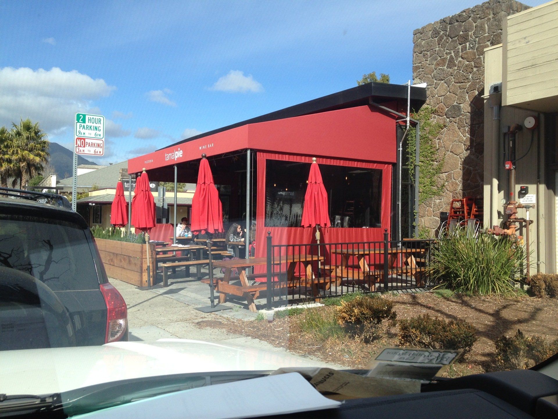 A white car is parked in front of a restaurant with red umbrellas