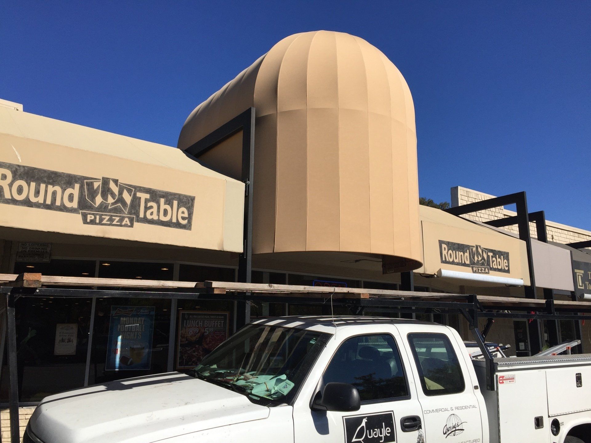 A white truck is parked in front of a building that says round table pizza