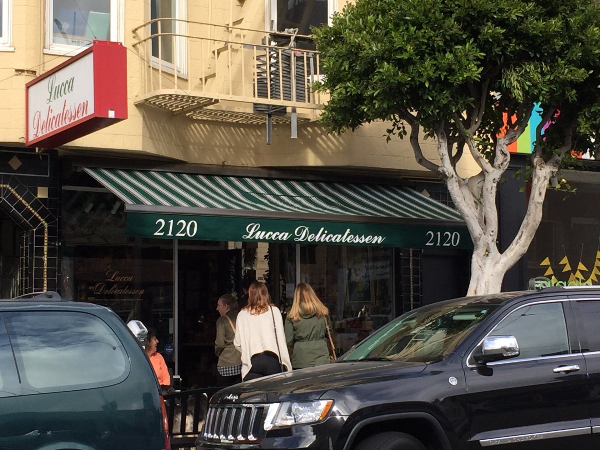 A group of people are standing outside of a restaurant with a green and white awning.