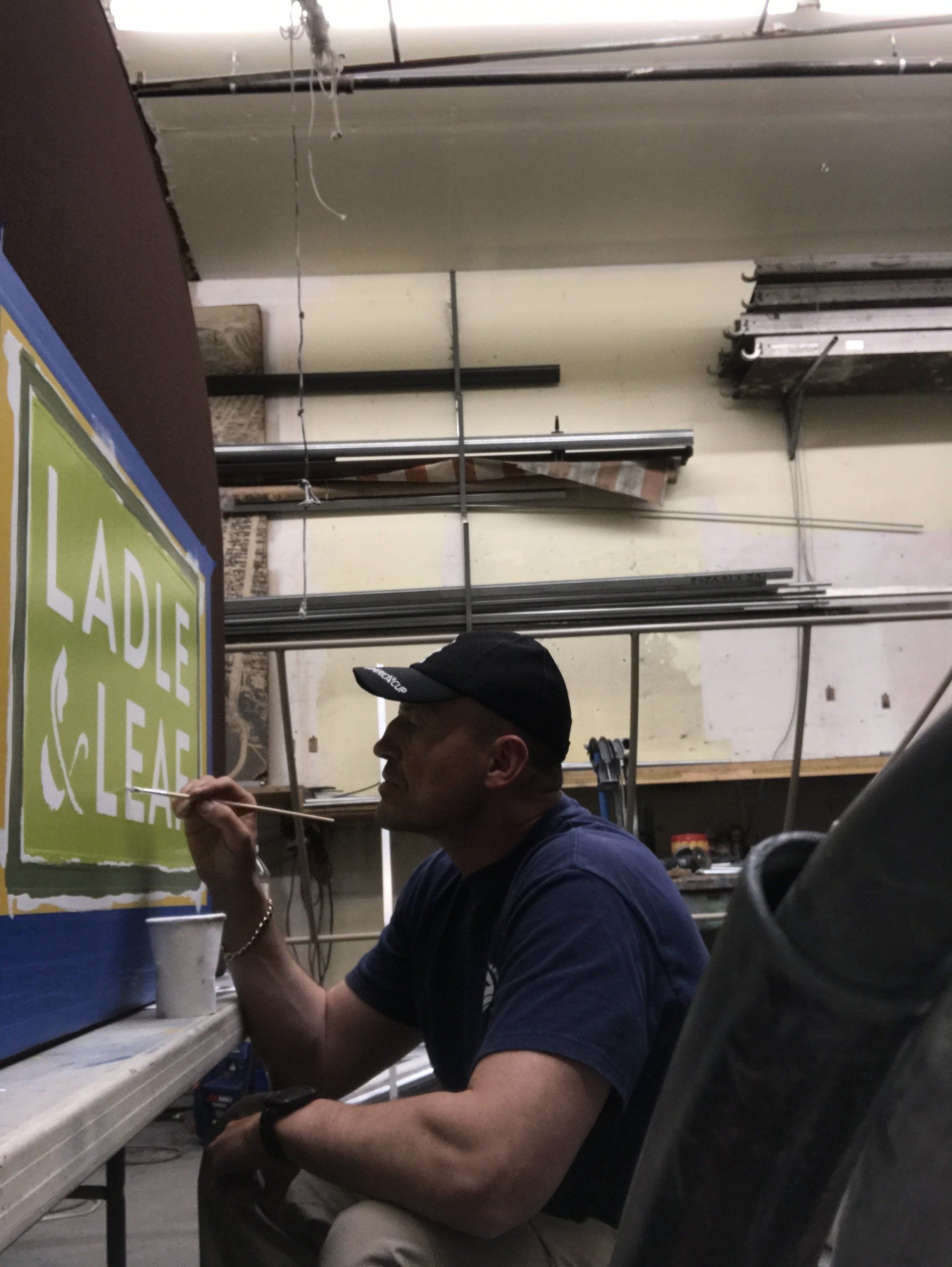 A man is painting a sign that says ladle & leaf