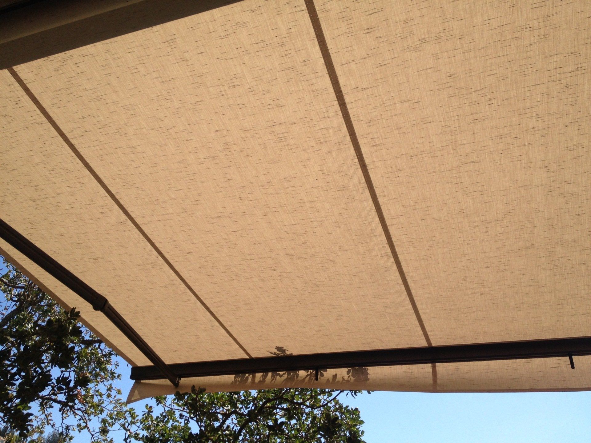 A tan awning is hanging from a roof with trees in the background