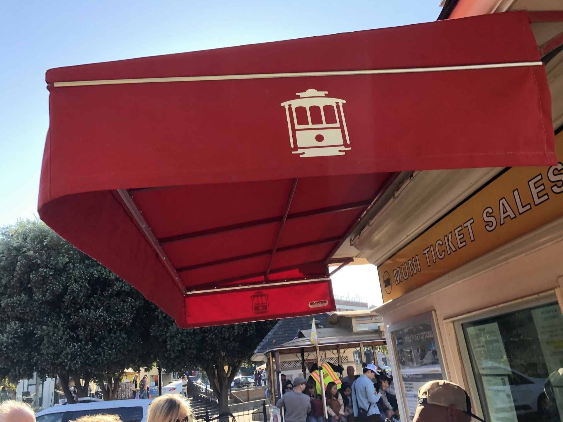 A group of people are standing under a red awning that says ticket sales