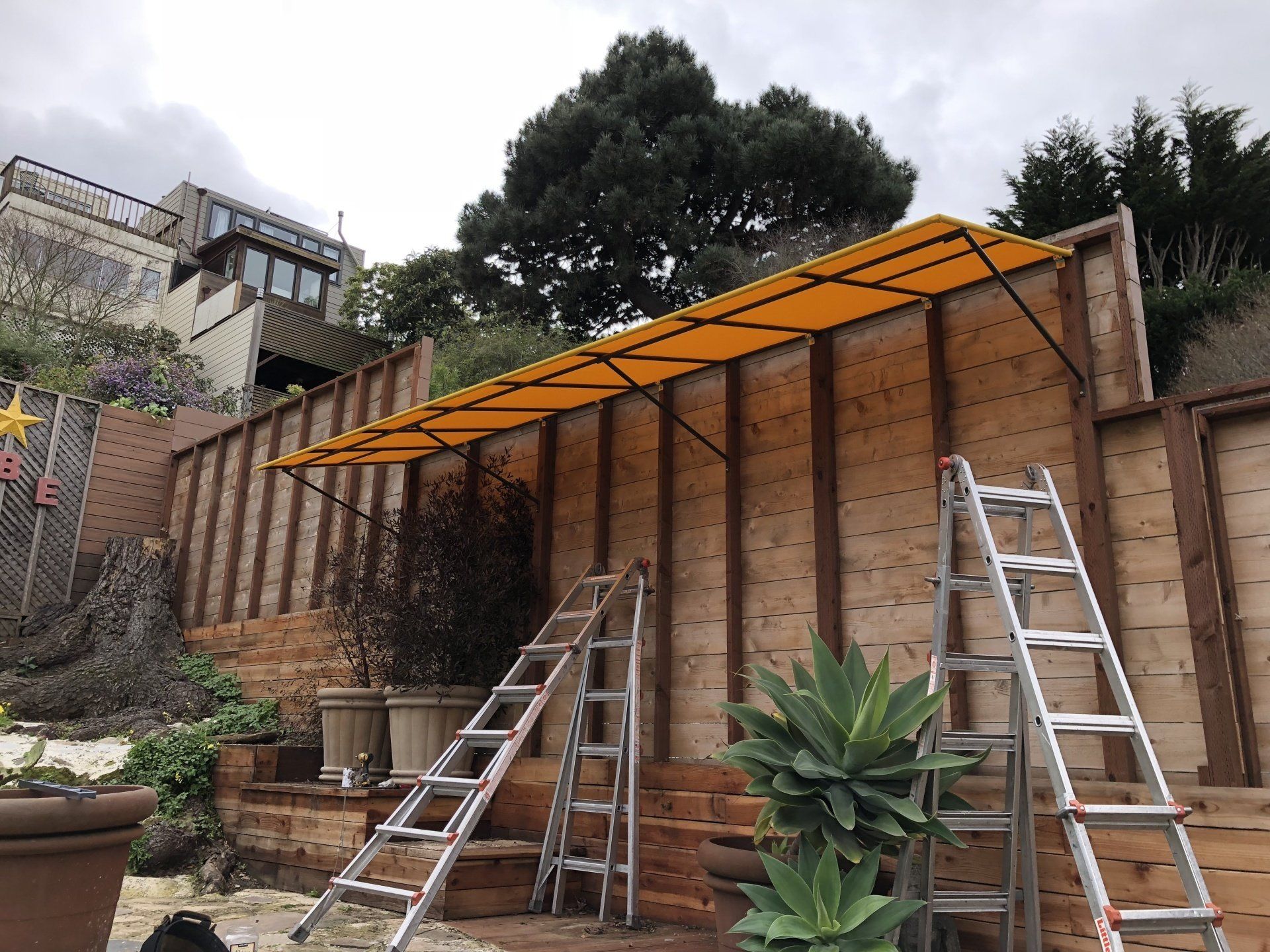 Two ladders are sitting next to a wooden fence.