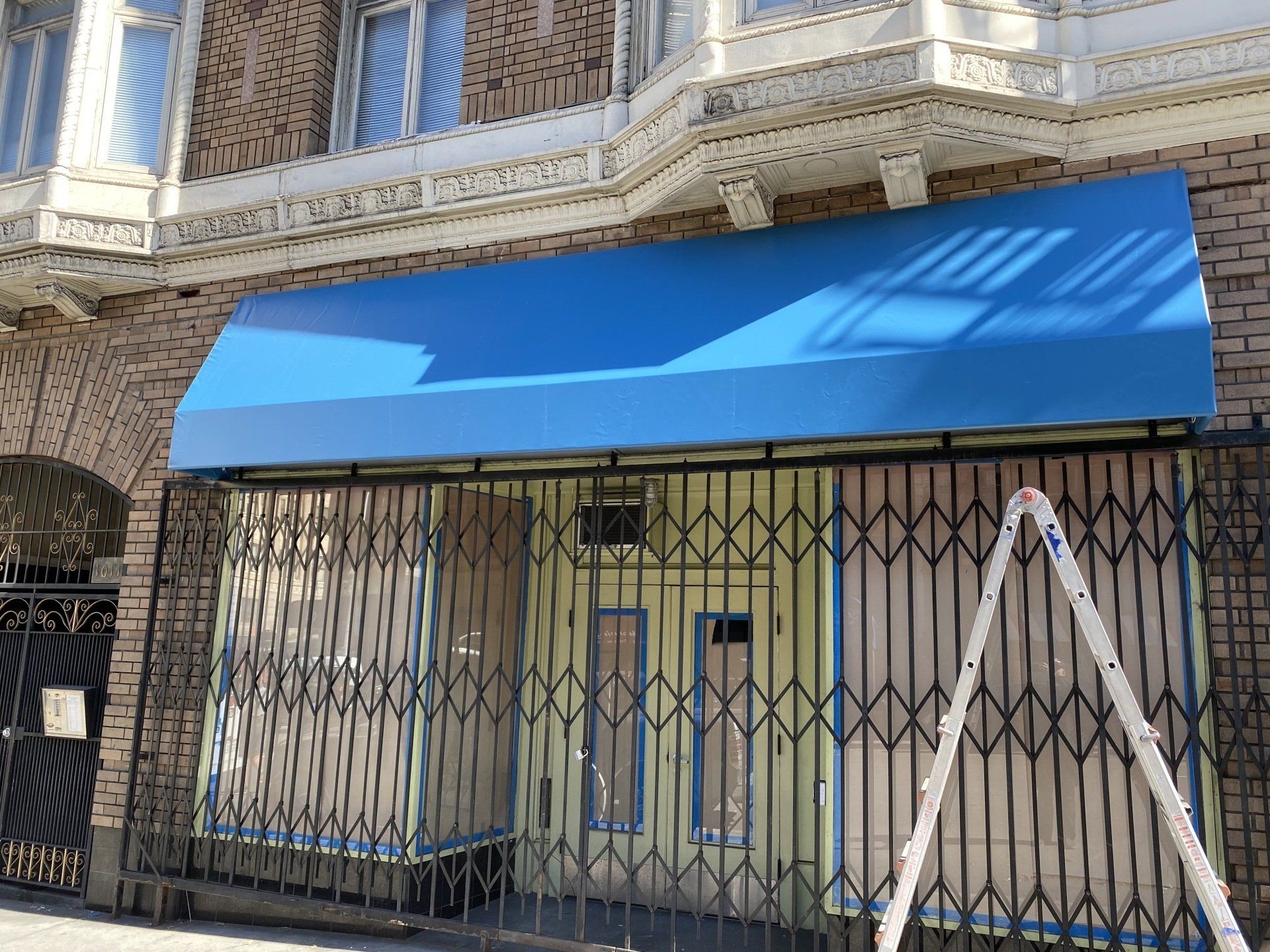 A building with a blue awning and a ladder in front of it.