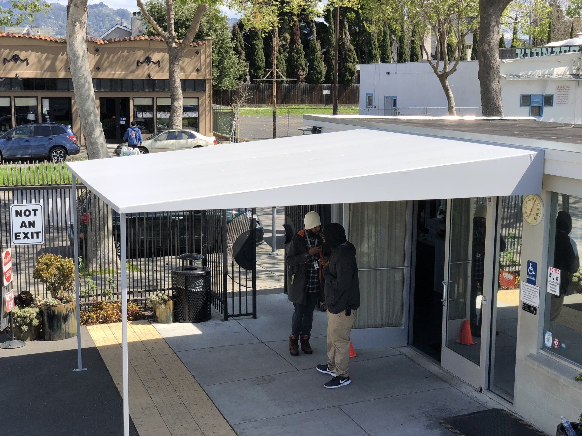 A group of people are standing under a canopy in front of a building.