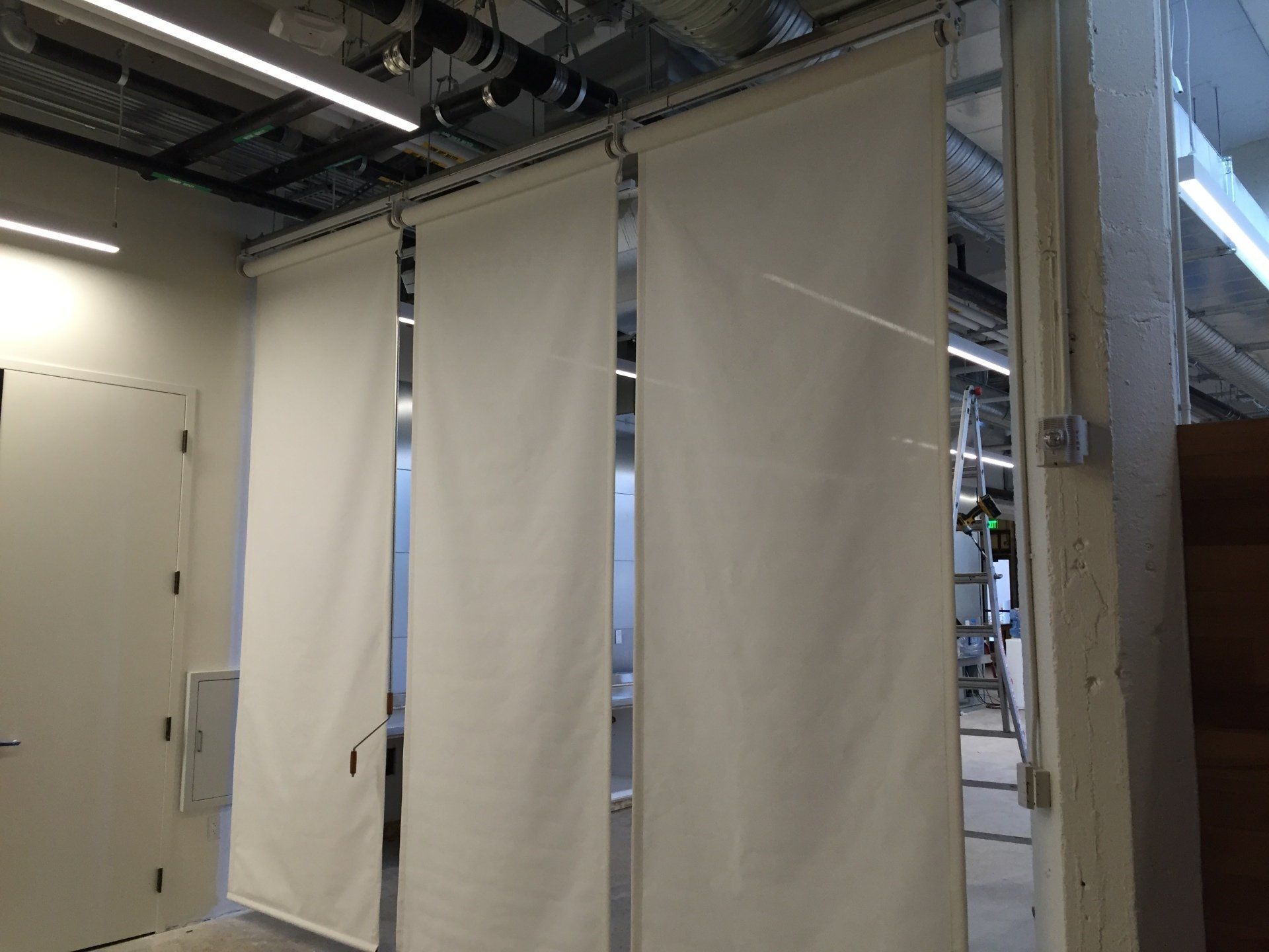 Three white curtains are hanging on a wall in a room.