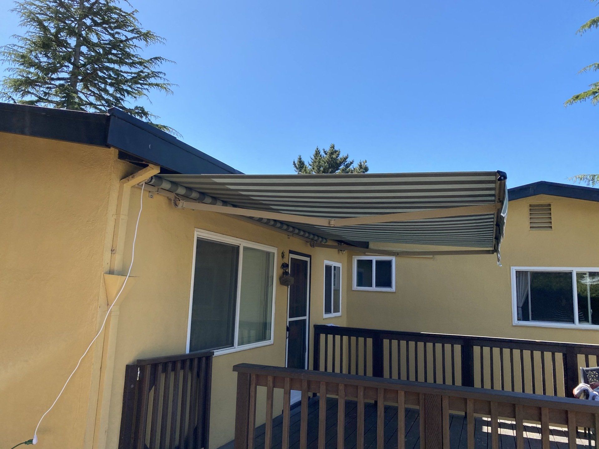 A yellow house with a wooden deck and an awning over it.