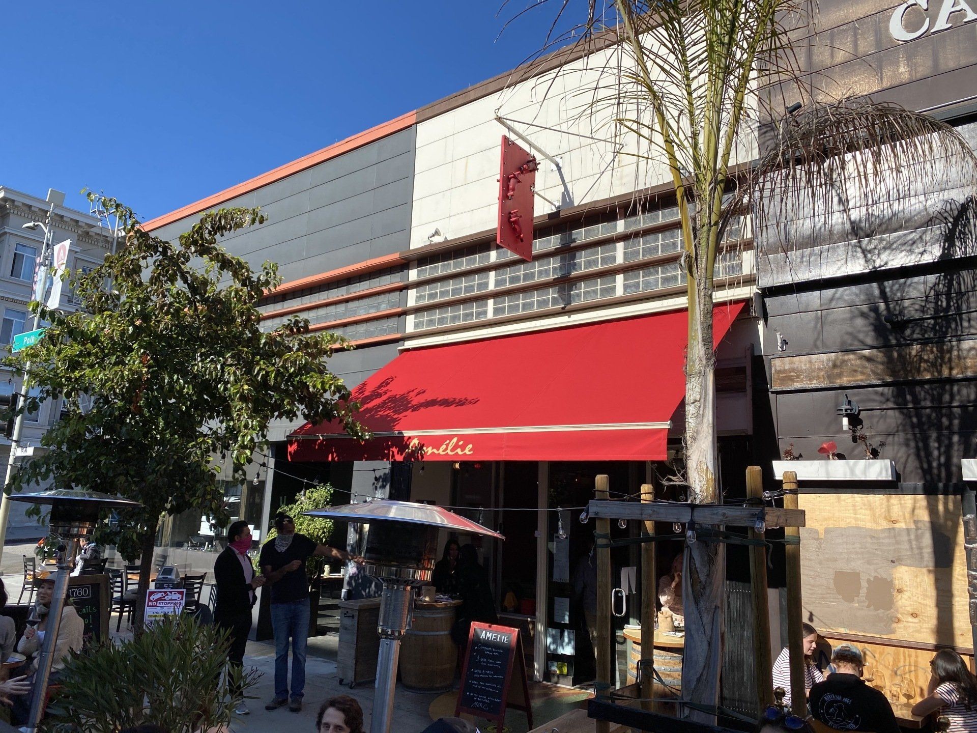 A restaurant with a red awning and people sitting outside