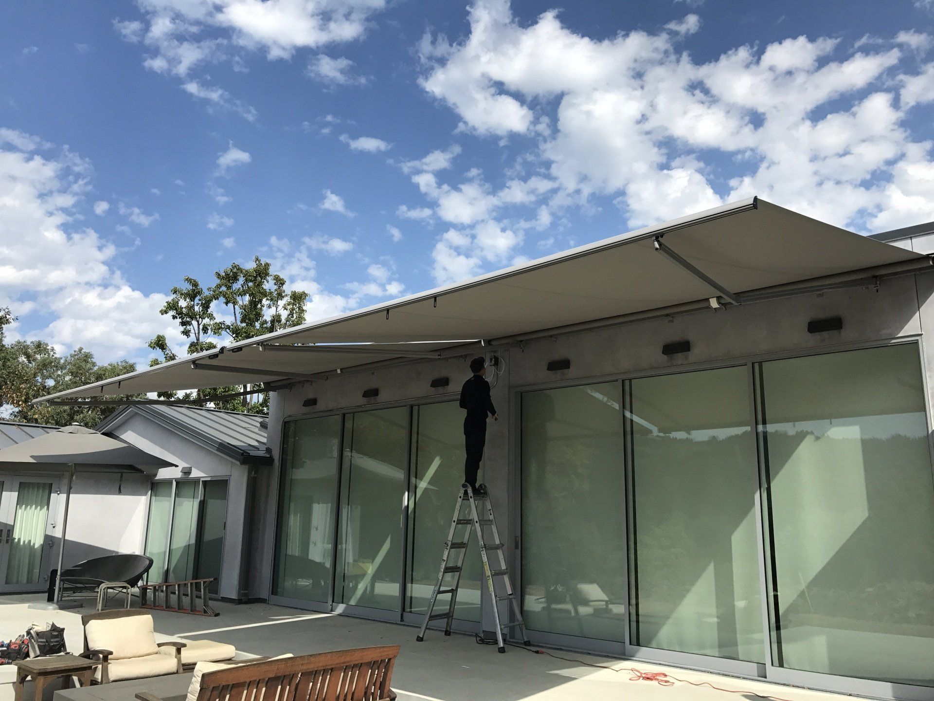 A man is standing on a ladder under an awning on the side of a house.