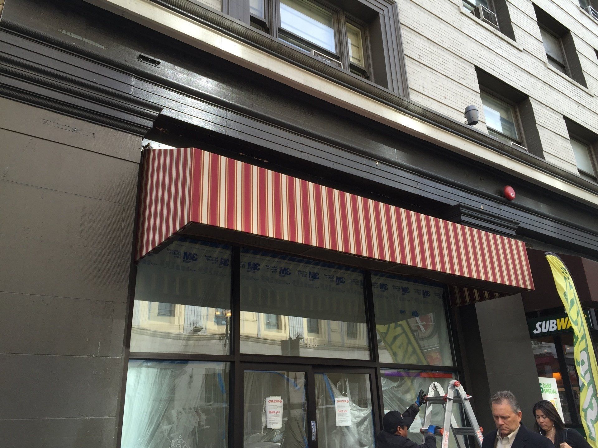 A red and white awning is being installed on the side of a building