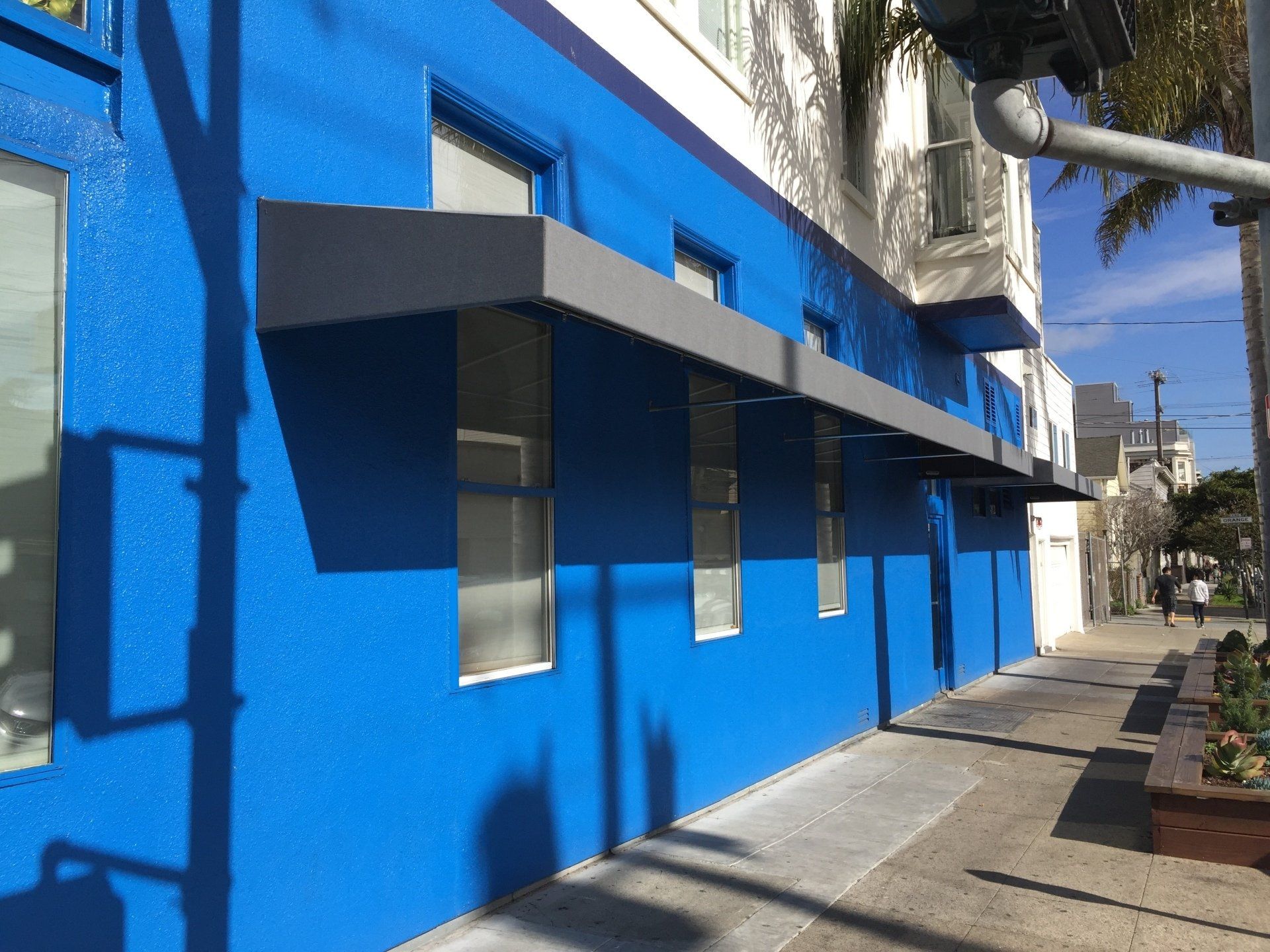 A blue building with a gray awning on the sidewalk