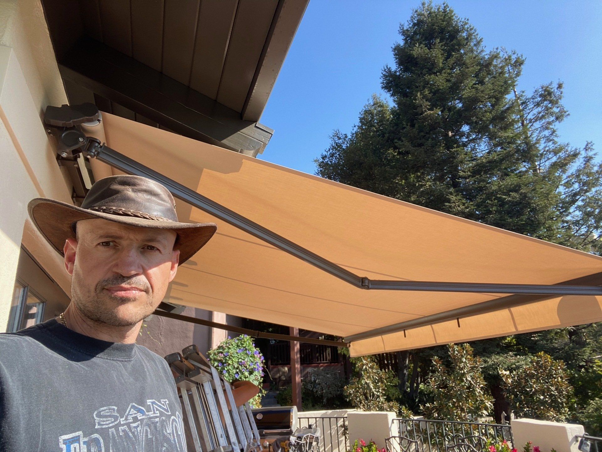 A man in a hat is standing under an awning on a porch.