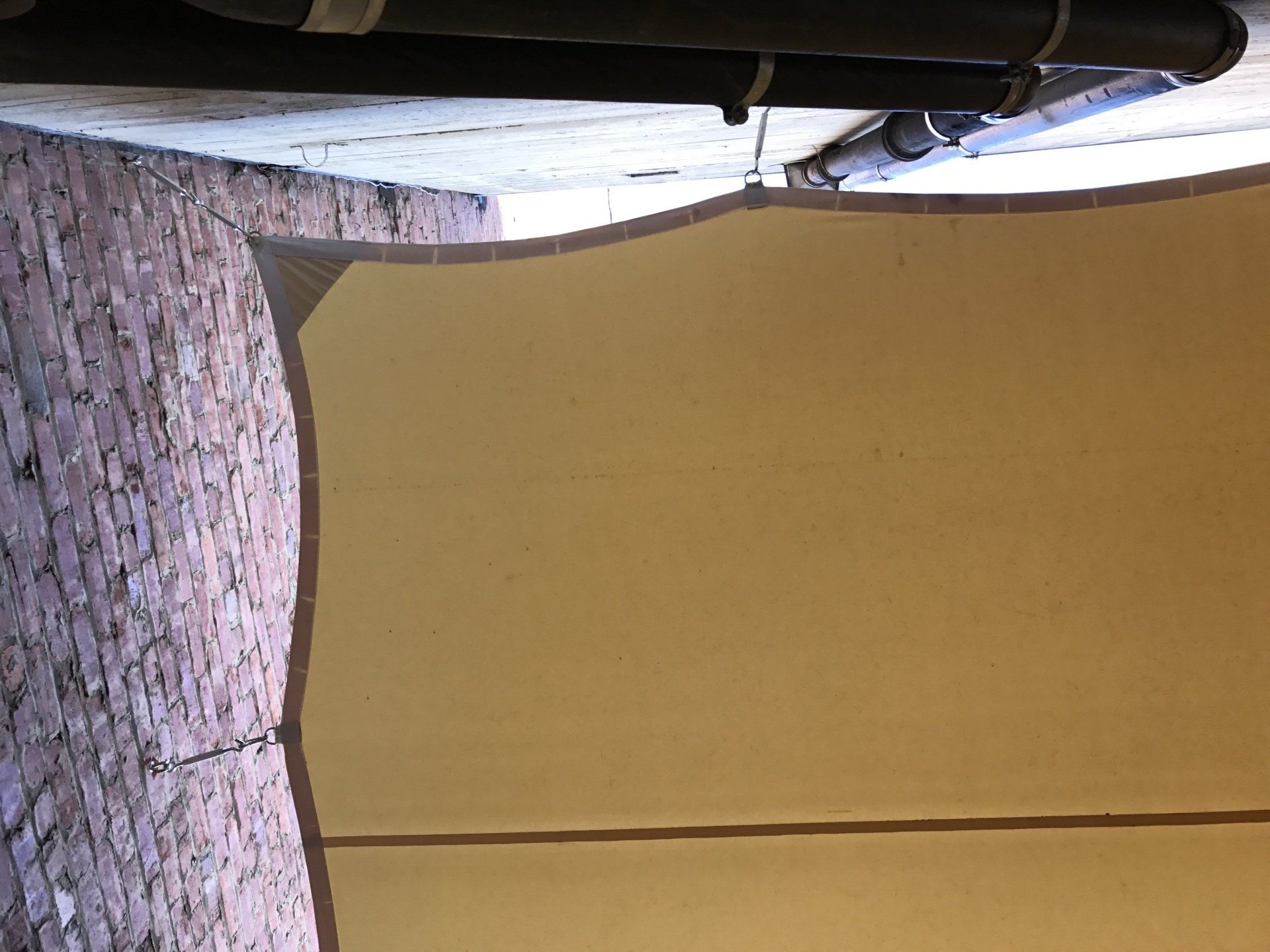 A drain pipe is hanging from the ceiling above a brick wall.