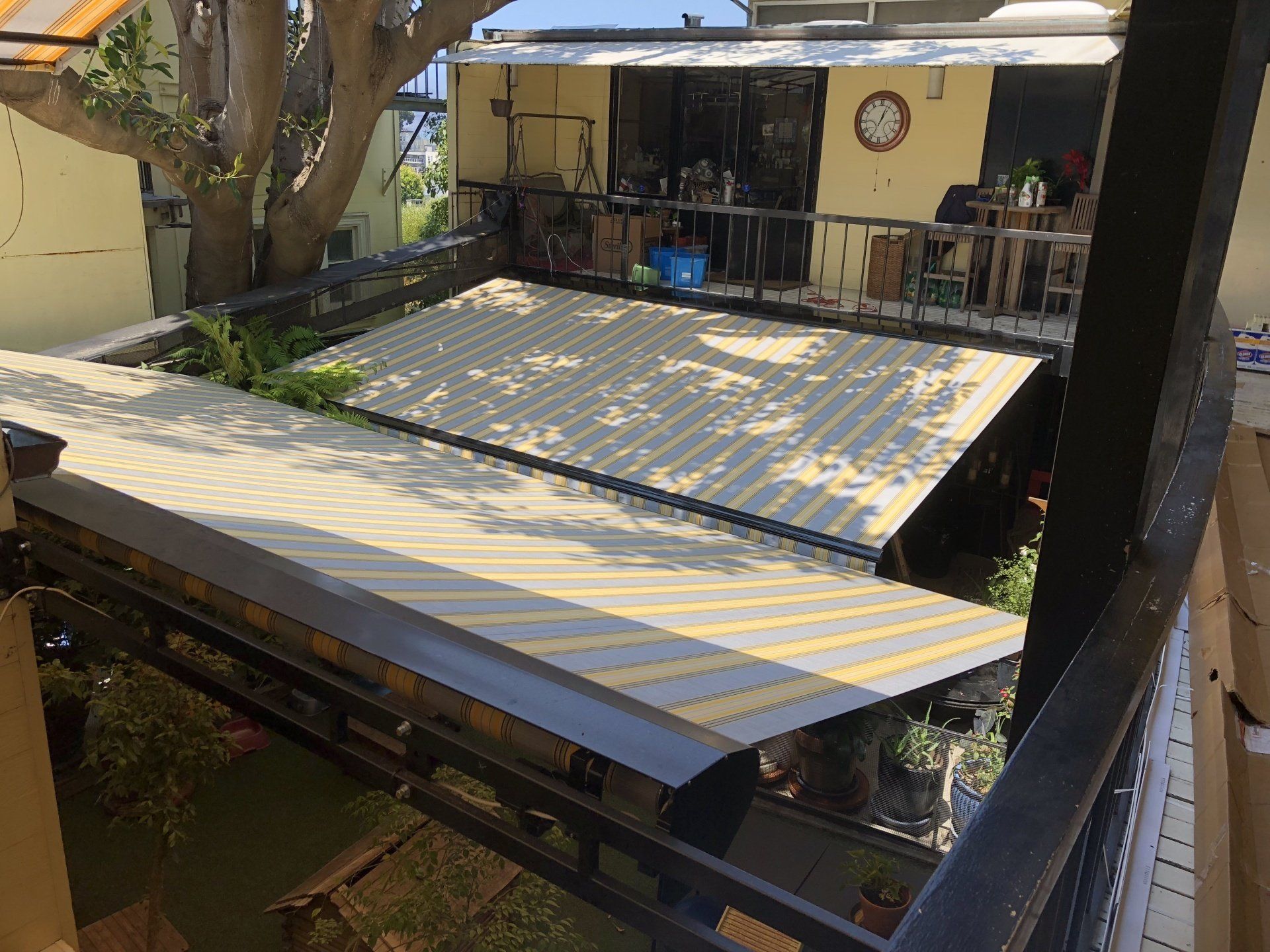 A balcony with a striped awning on it and a tree in the background.