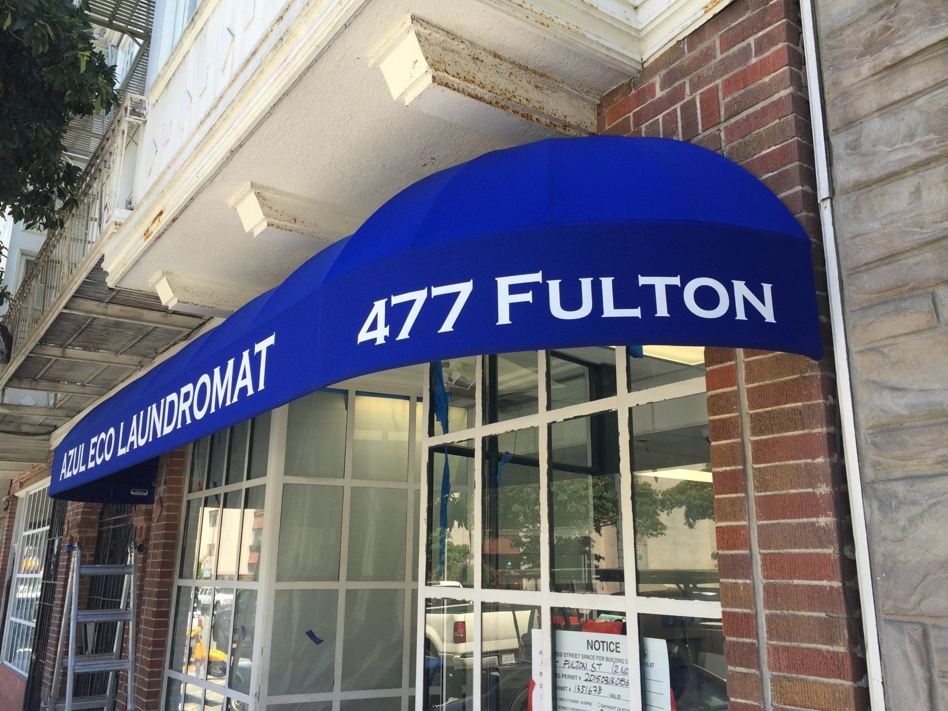 A blue awning on the side of a building that says 477 fulton