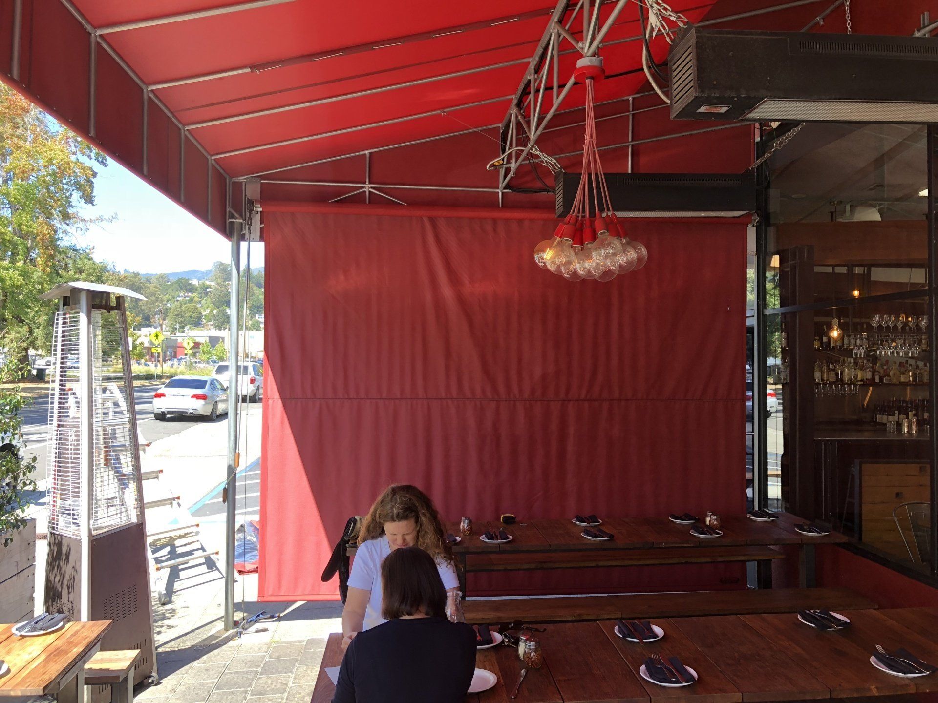 A group of people are sitting at tables under a red awning.