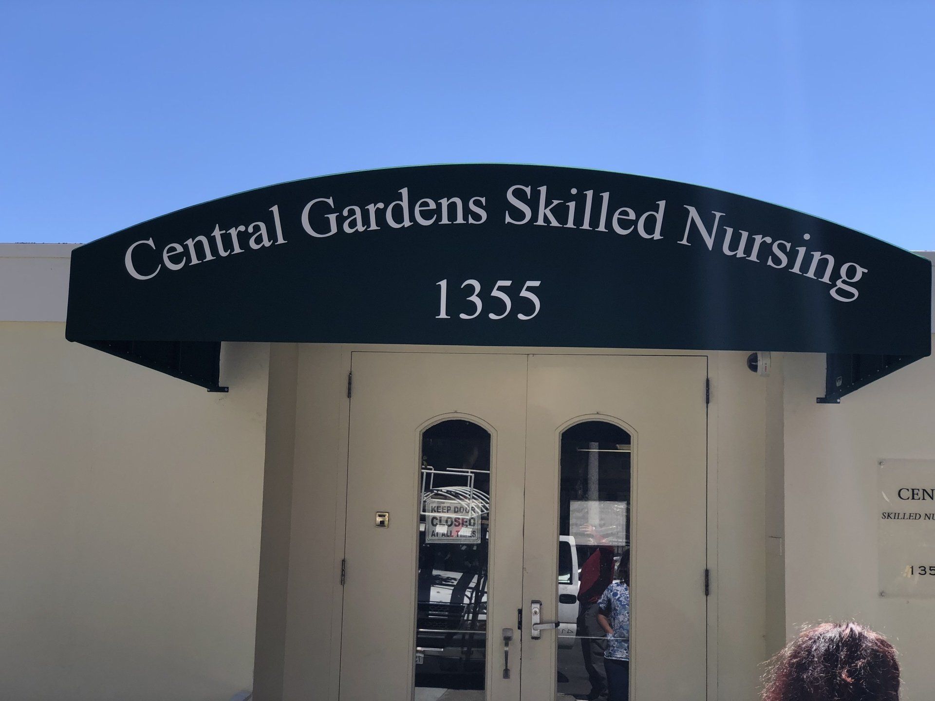 A woman stands in front of a building that says central gardens skilled nursing