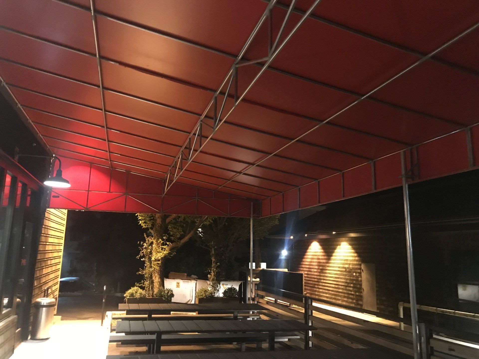 A red awning over a patio with tables and benches at night