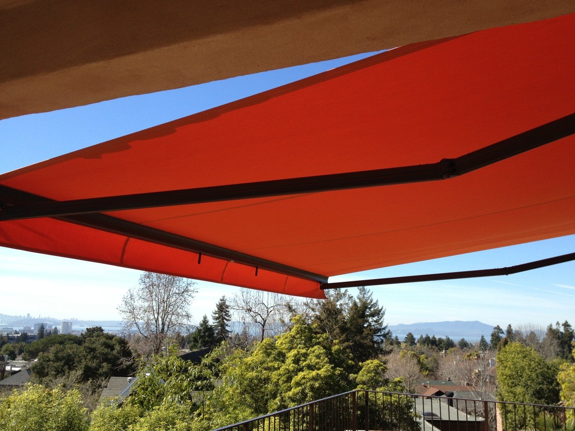 An orange awning is covering a balcony with trees in the background