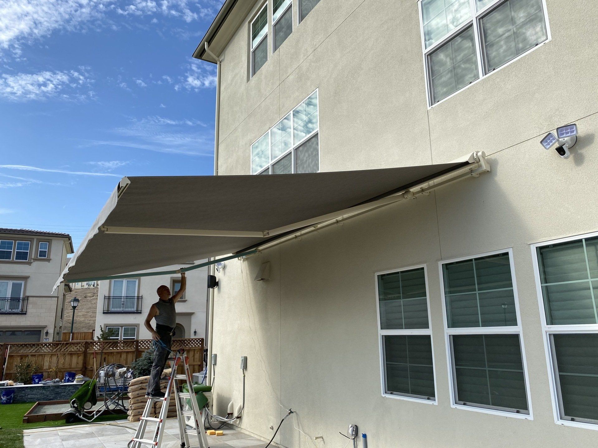 A man is installing an awning on the side of a house.