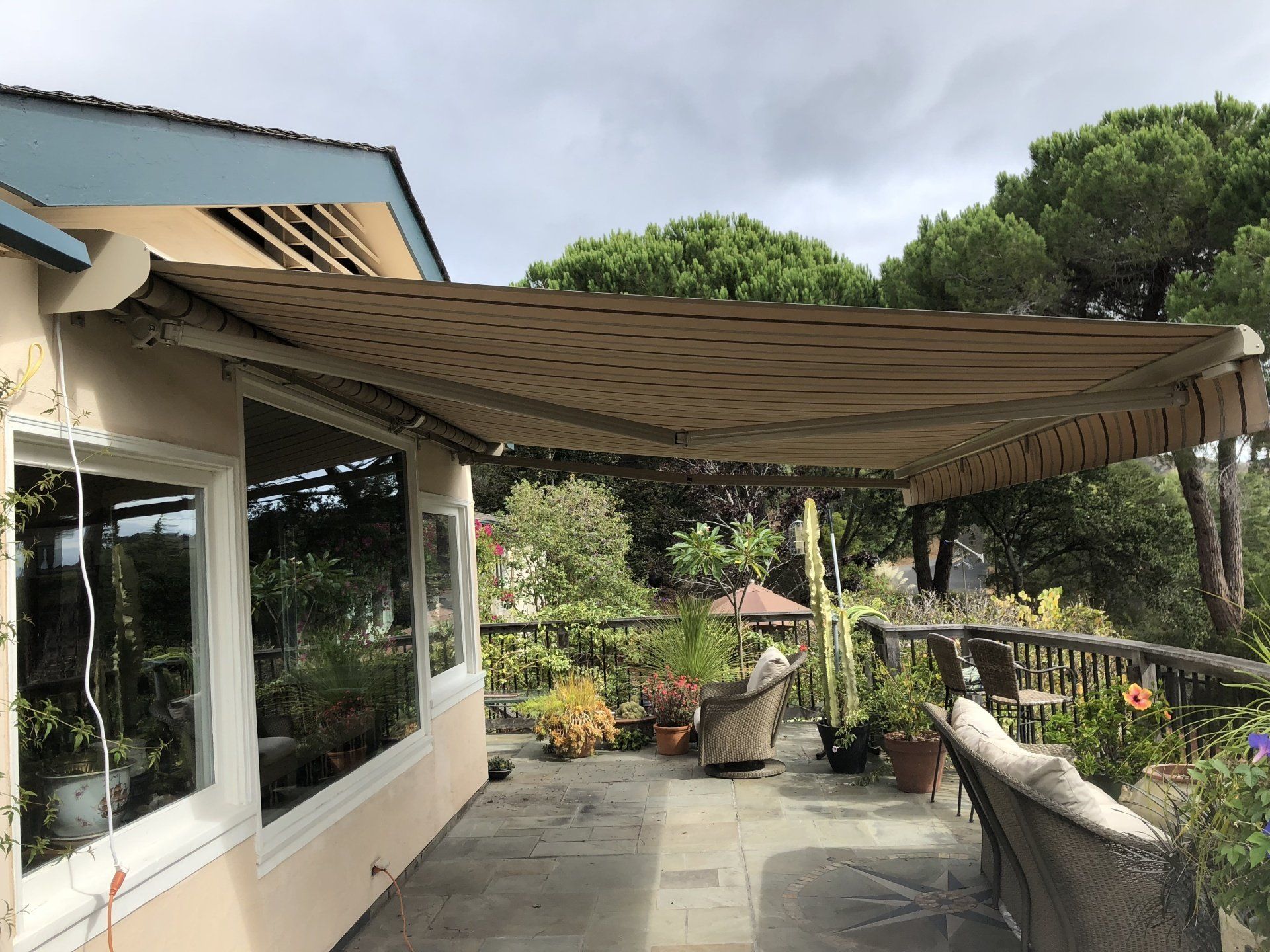 A large awning is covering a patio with chairs and plants.