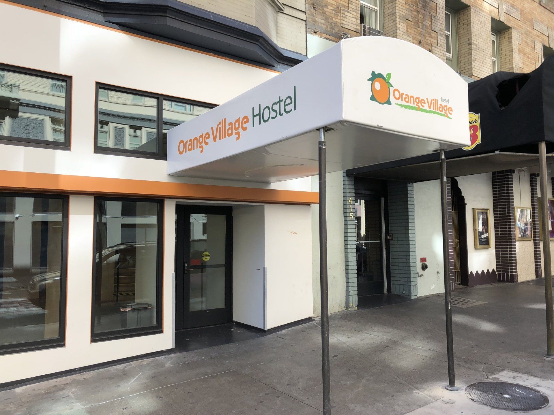 A white building with a canopy that says orange village hostel