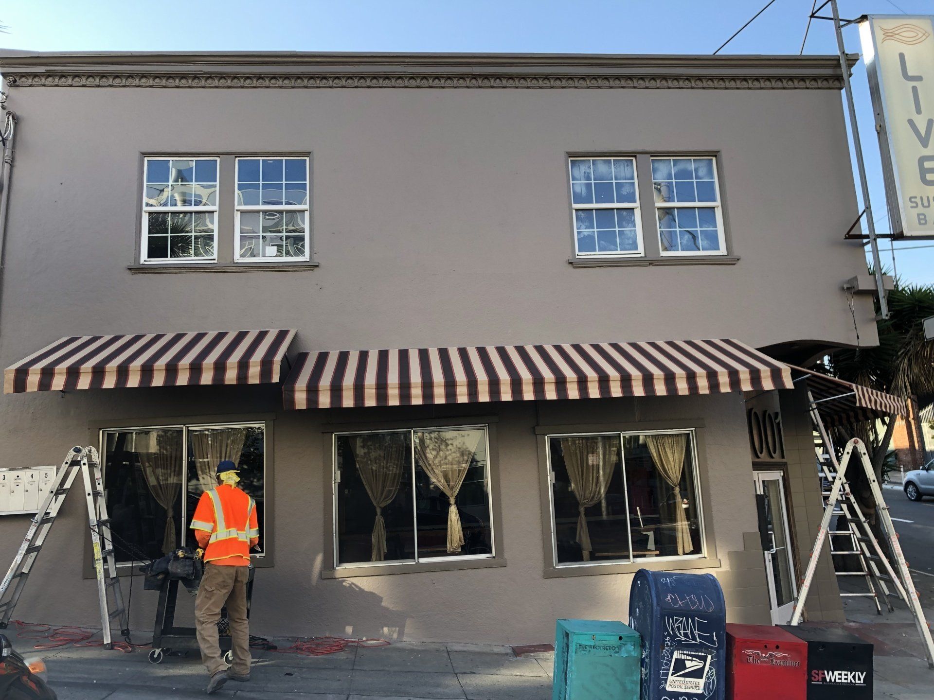 A man is standing in front of a building with a striped awning.