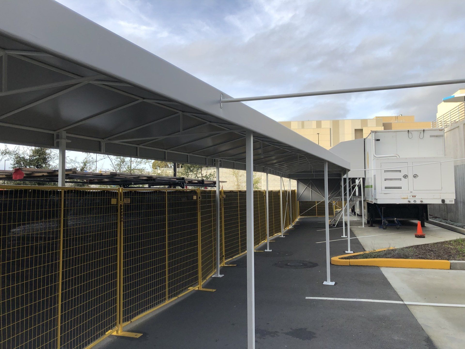 A covered walkway with a fence and a truck in the background.