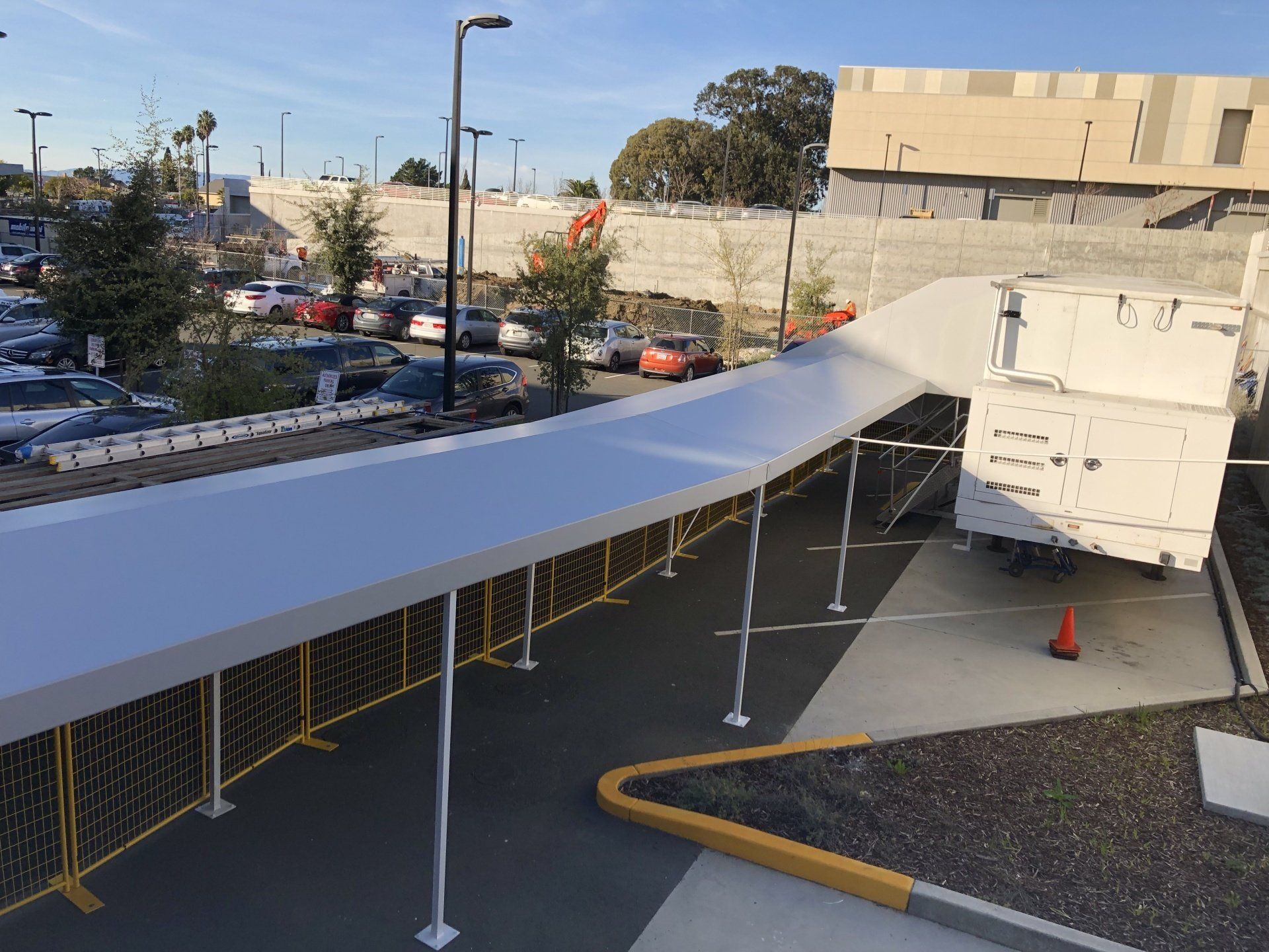 A white truck is parked under a white canopy in a parking lot.