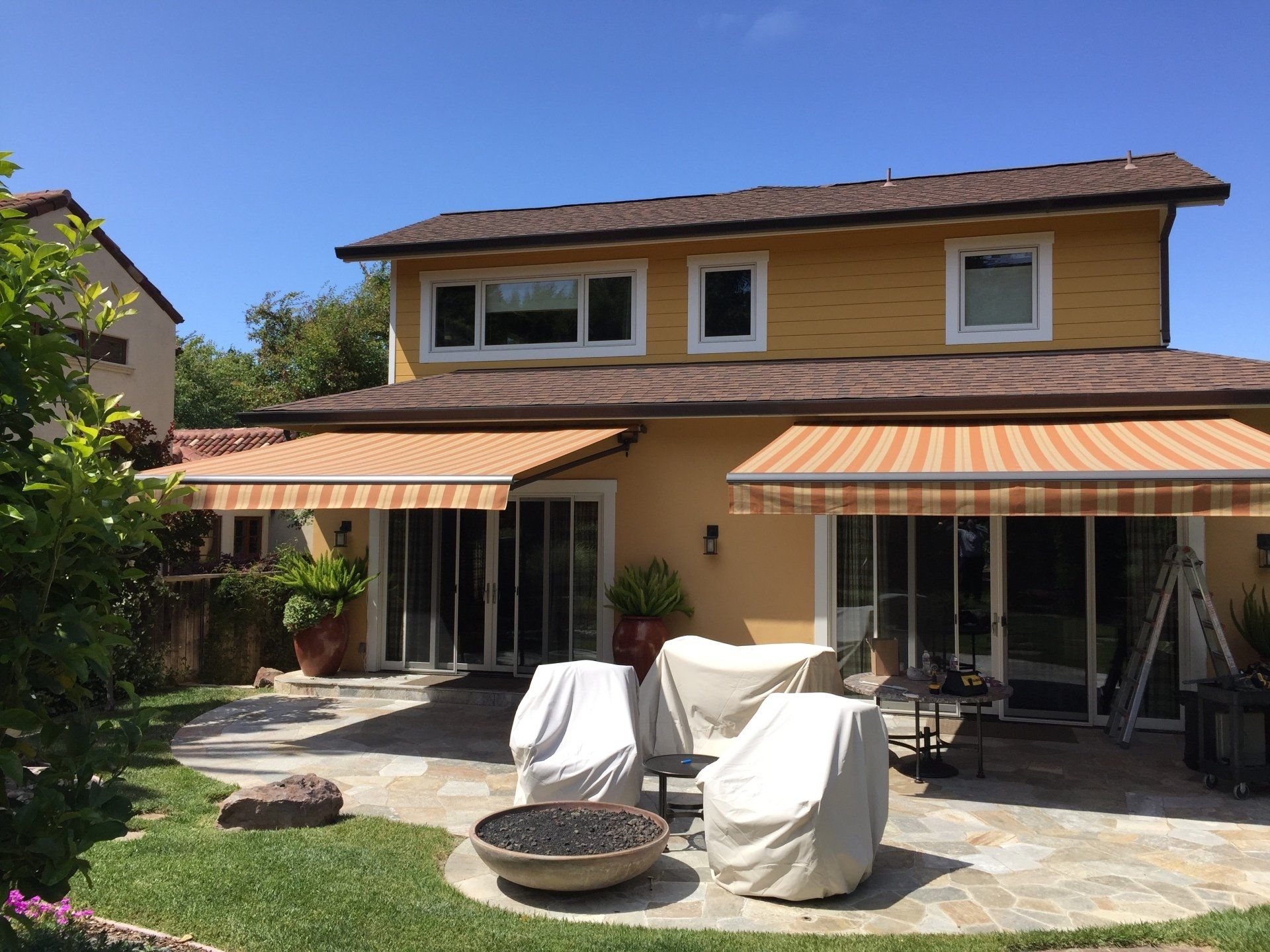 The backyard of a house with a striped awning and a fire pit.