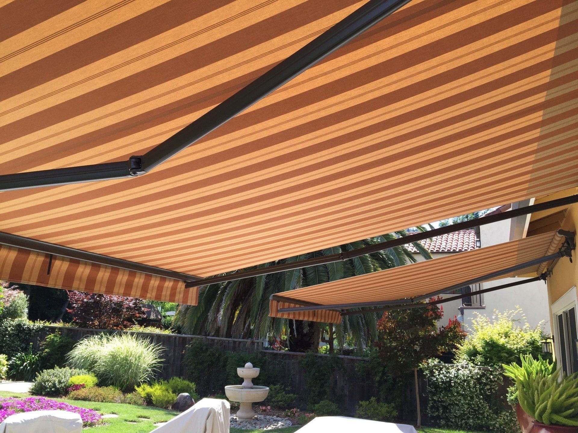 A striped awning is covering a patio with a fountain in the background