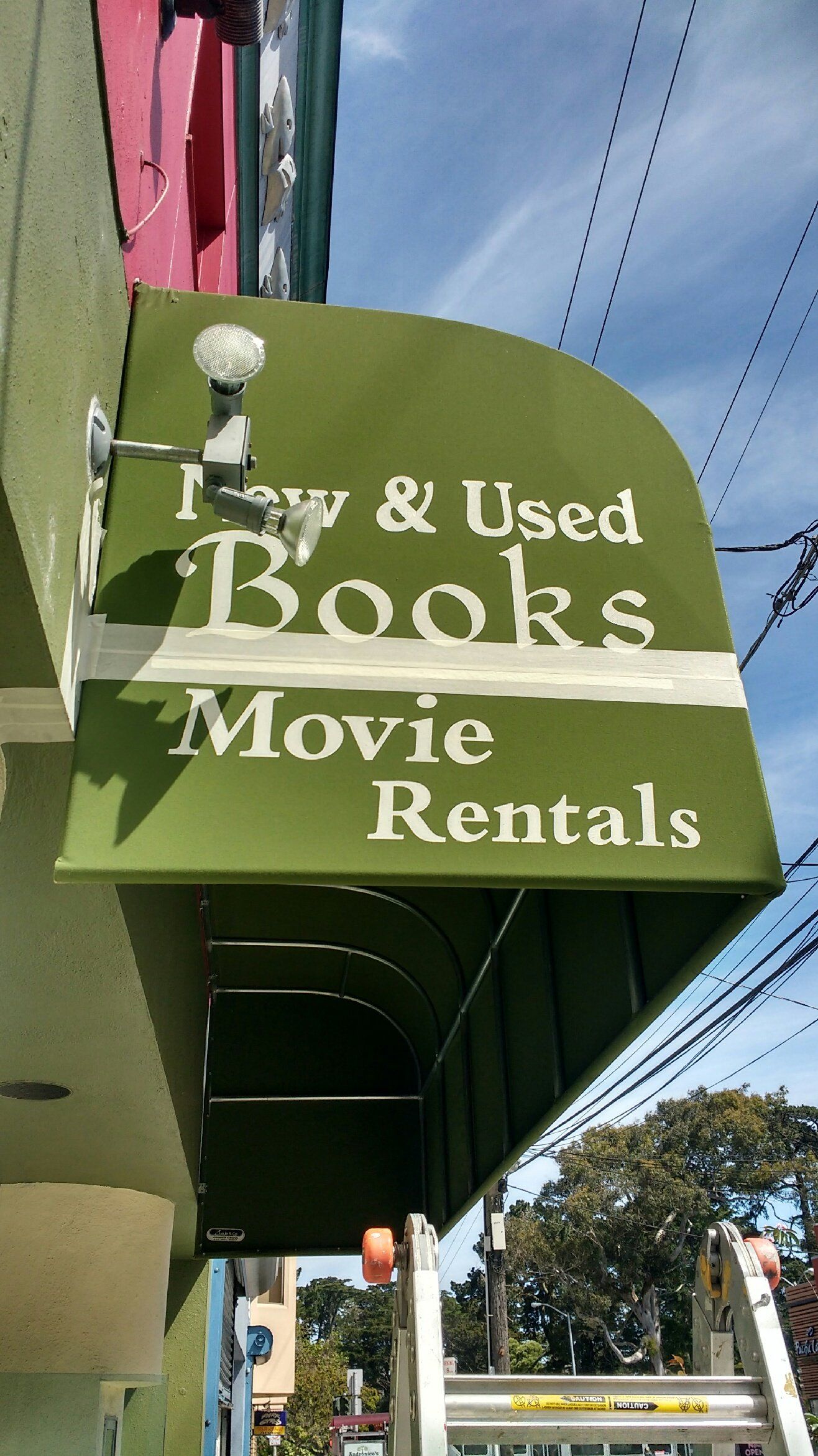 A green awning on the side of a building advertising new and used books and movie rentals.