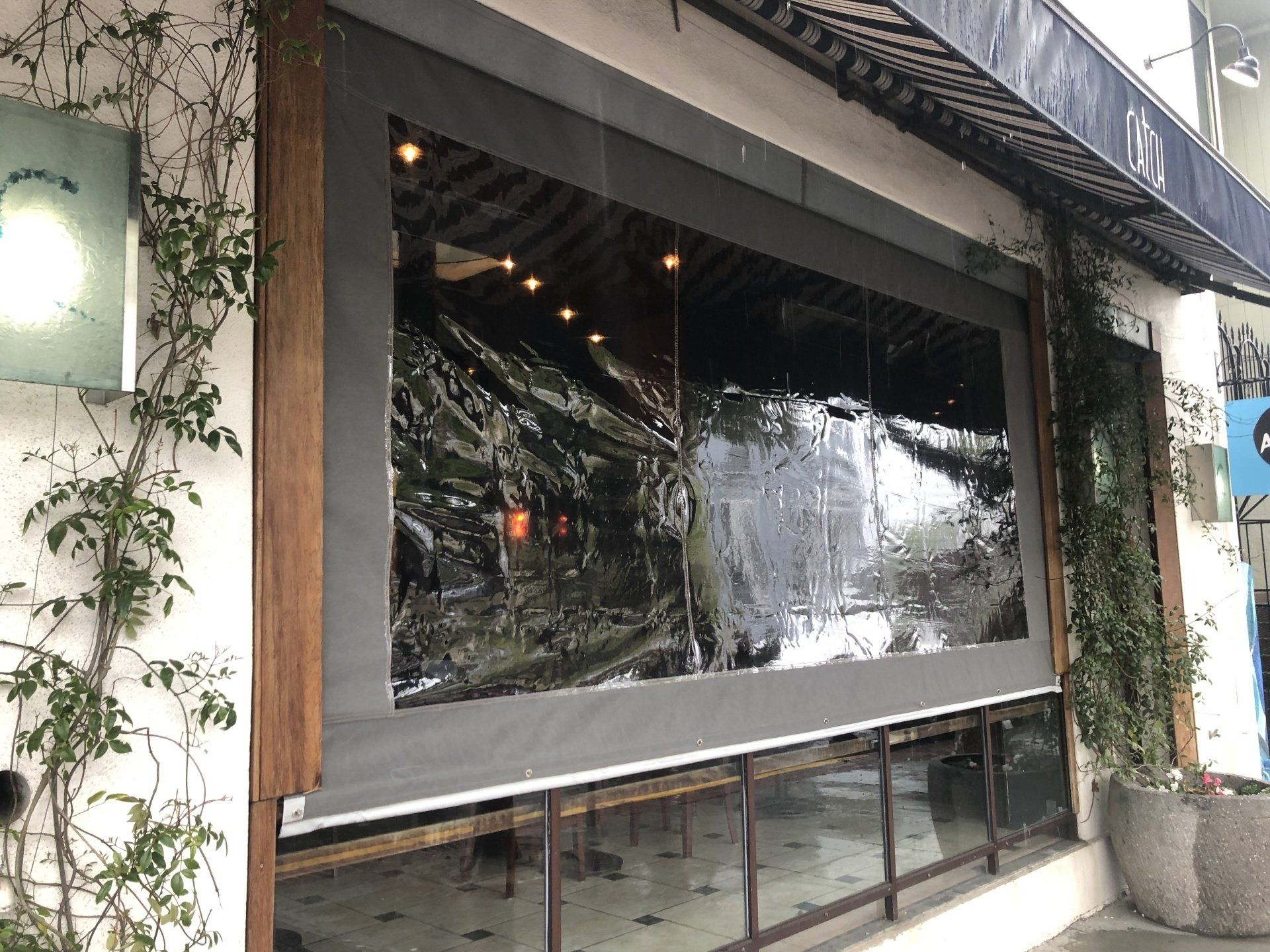 A restaurant with a large window and a gray awning.