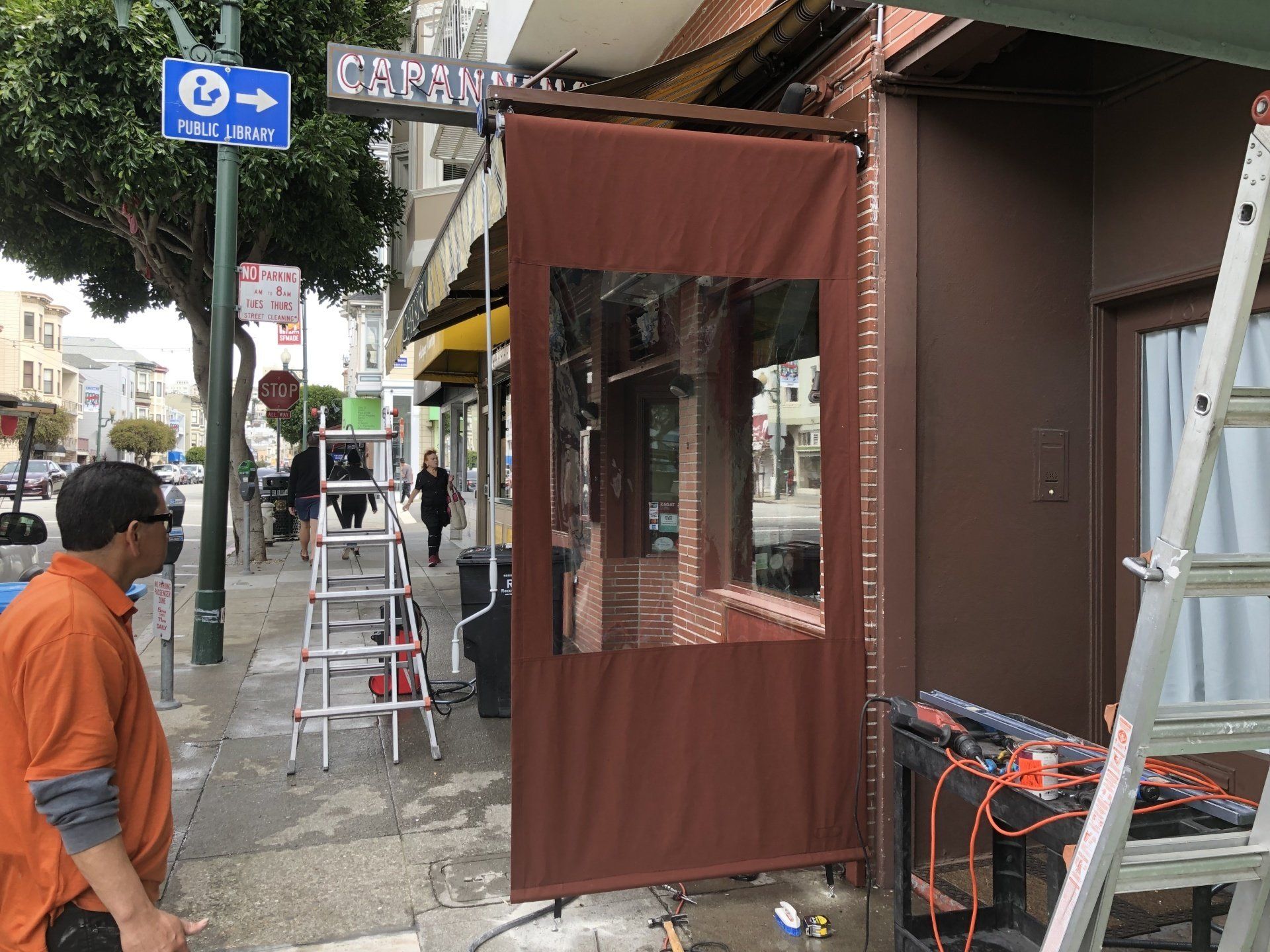A man is standing on a sidewalk next to a ladder.