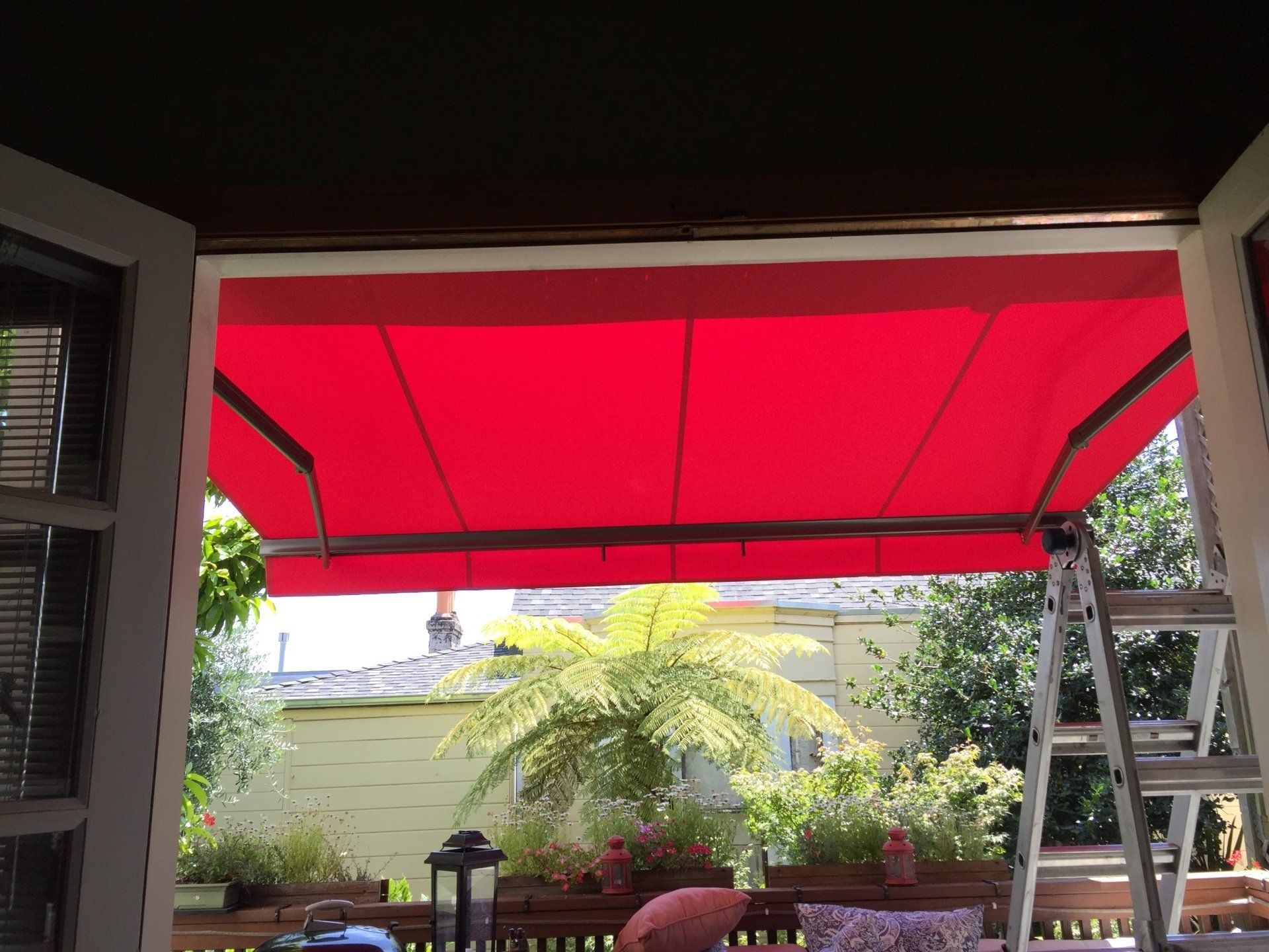 A red awning is hanging over a patio with a ladder in the background.