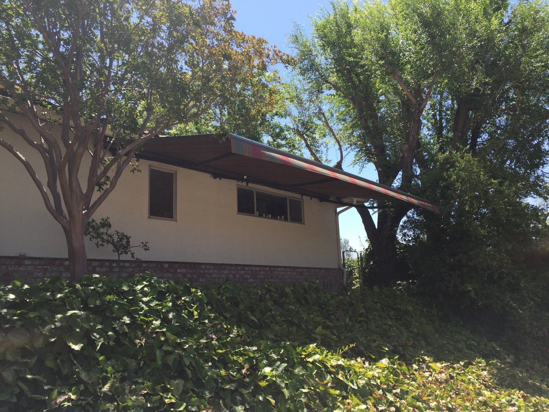 A white house with a red roof is surrounded by trees and bushes
