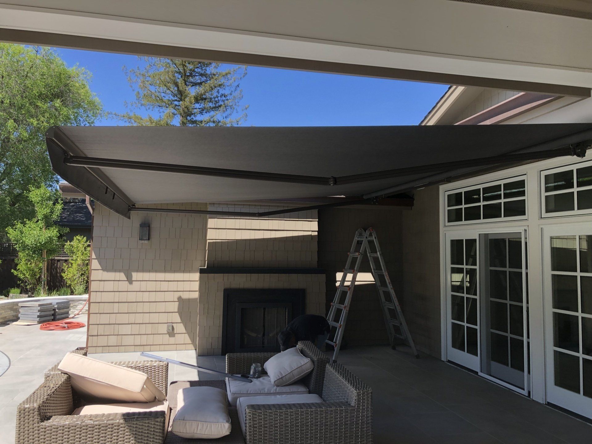 A patio with a couch , chairs and a fireplace under an awning.