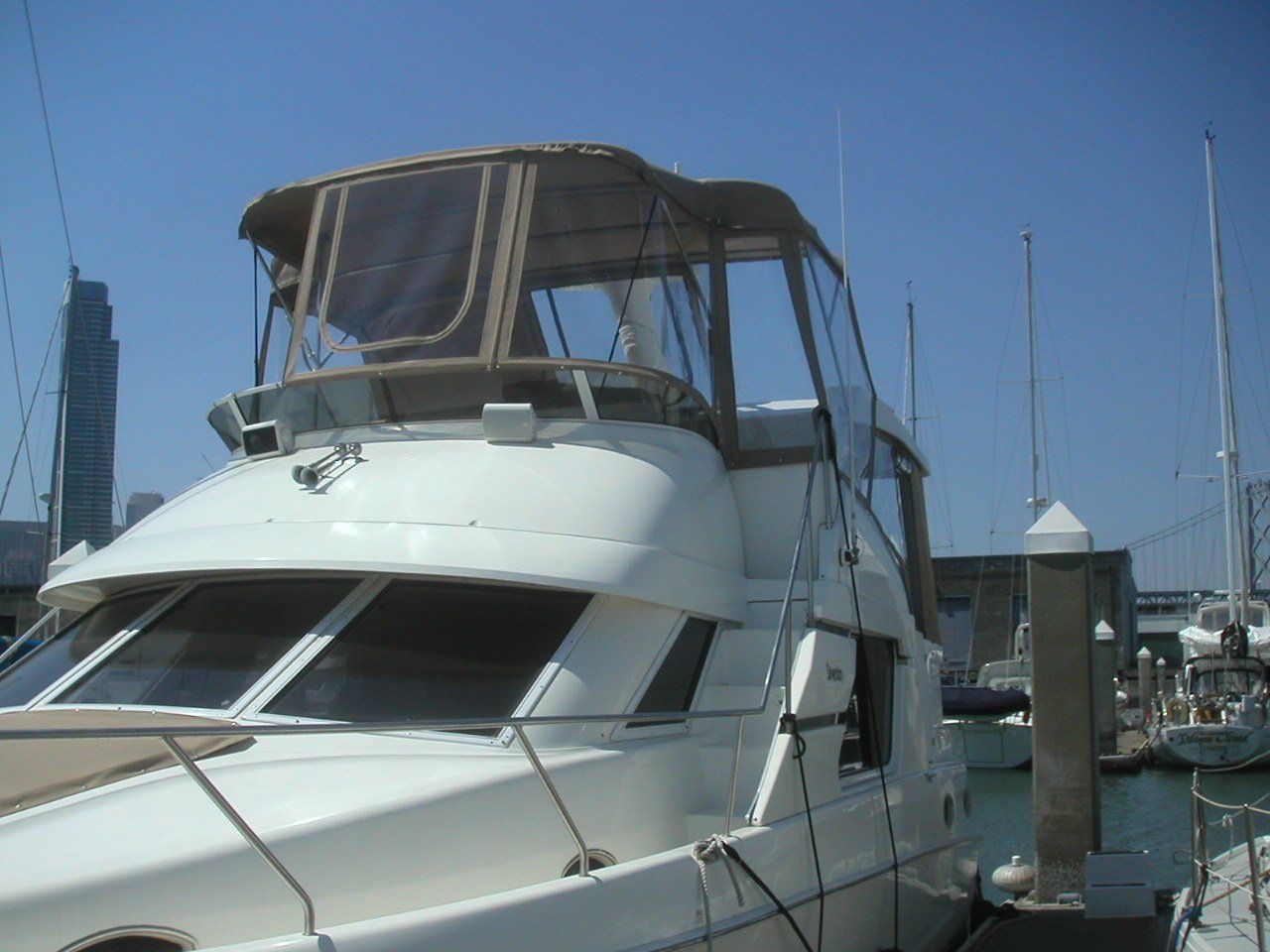 A white boat with a brown canopy is docked at a marina