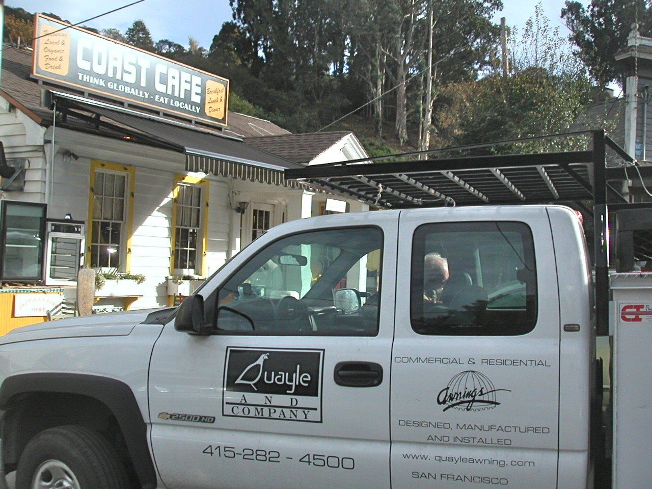 A white truck is parked in front of a building that says coast cafe