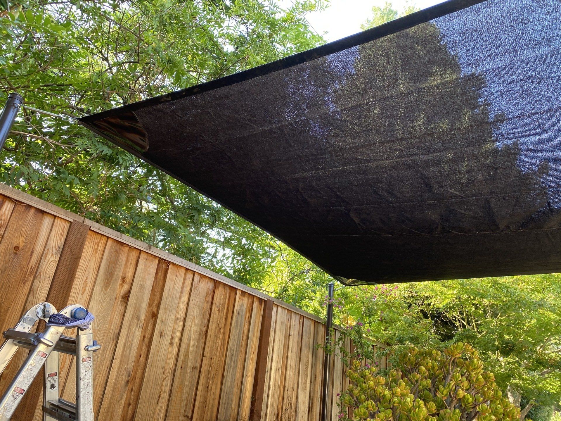 A ladder is leaning against a wooden fence under a black shade.