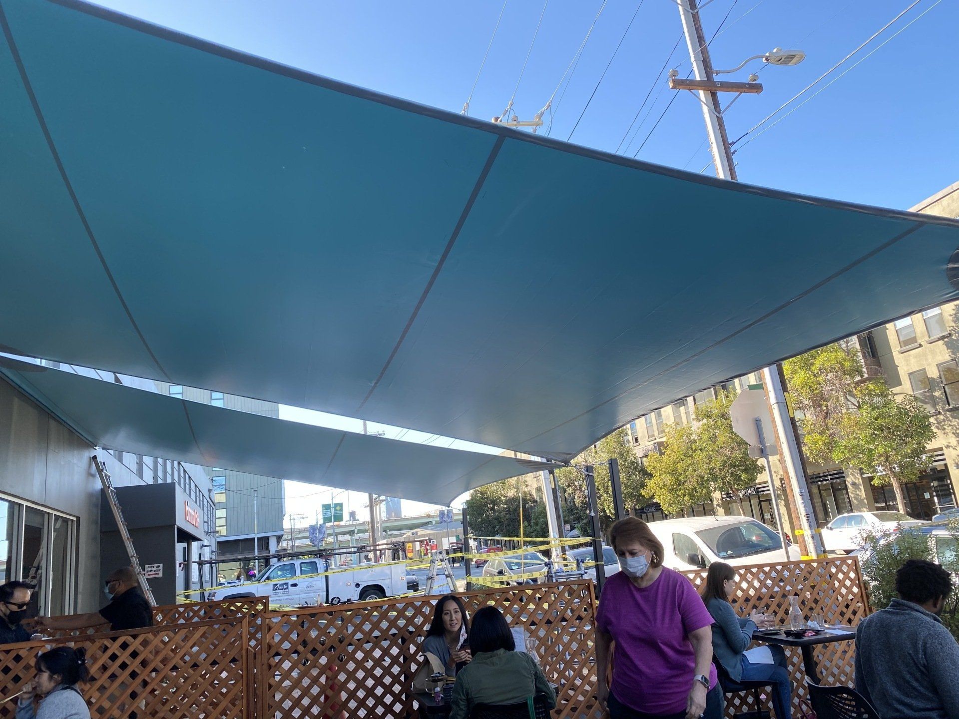 A group of people are sitting under a blue umbrella.