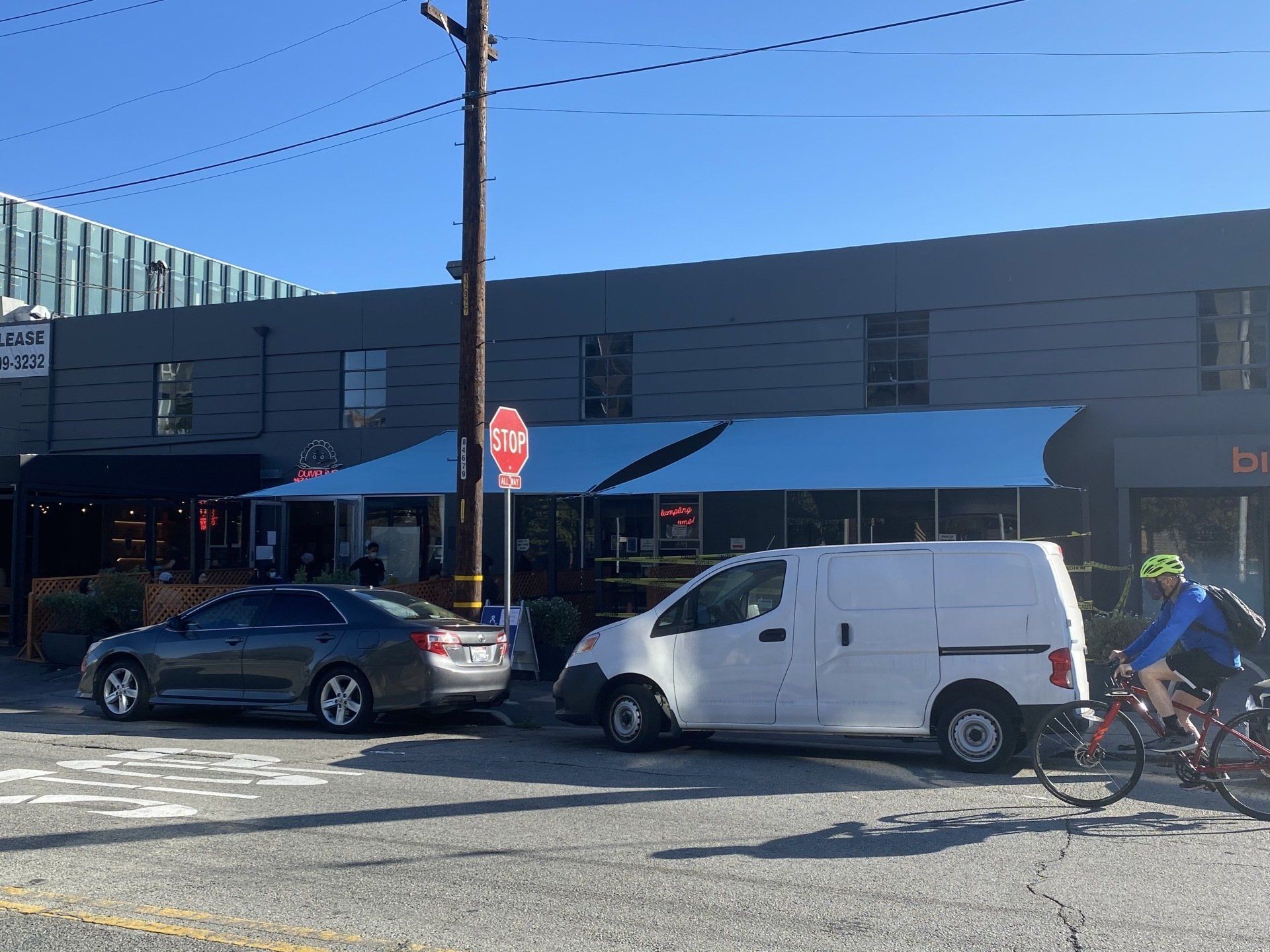 A man is riding a bike next to a white van parked in front of a building.