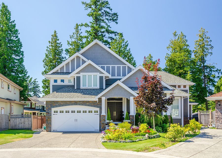 A large house with a white garage door is surrounded by trees.