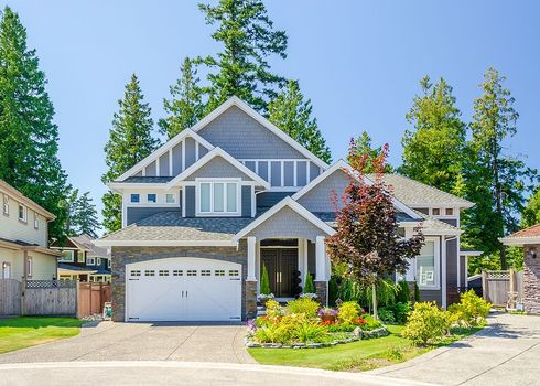 A large house with a white garage door is surrounded by trees.