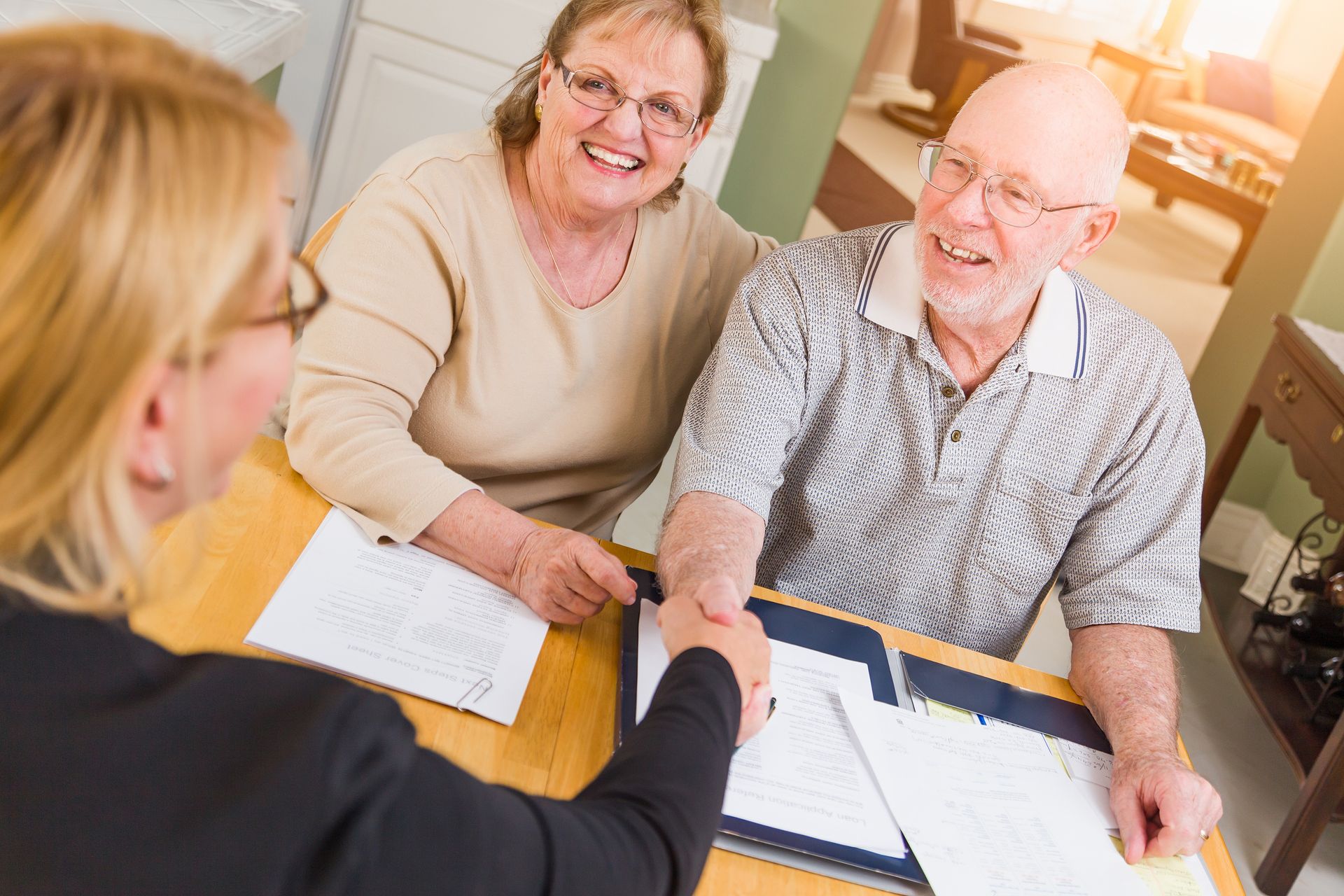 An elderly couple is shaking hands with a woman while sitting at a table.